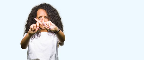Young beautiful girl with curly hair wearing casual white t-shirt Rejection expression crossing fingers doing negative sign - Photo, Image