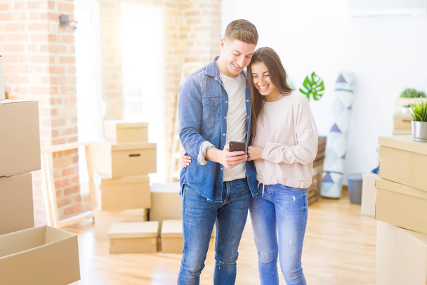 schönes junges Paar, das mit einem Smartphone in ein neues Haus zieht, mit einem glücklichen Gesicht im Stehen und einem selbstbewussten Lächeln, das Zähne zeigt - Foto, Bild