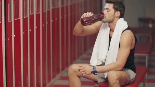 Вымотанный крупным планом мужчина сидит в гримерке со спортивной бутылкой
. - Кадры, видео
