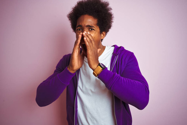 Młody African American Man ubrany w purpurową bluzę stojący na białym tle różowy Shouting zły na głos z rąk nad usta - Zdjęcie, obraz