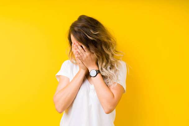 Young beautiful blonde woman over yellow background with sad expression covering face with hands while crying. Depression concept. - Fotoğraf, Görsel