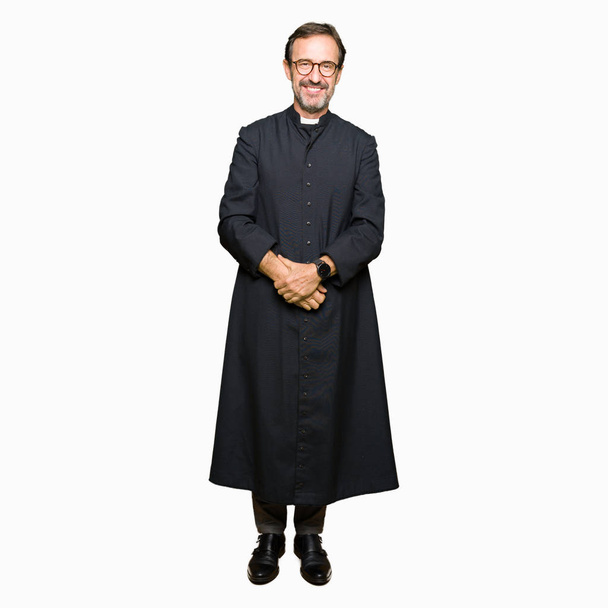 Middle age priest man wearing catholic robe Hands together and fingers crossed smiling relaxed and cheerful. Success and optimistic - Valokuva, kuva