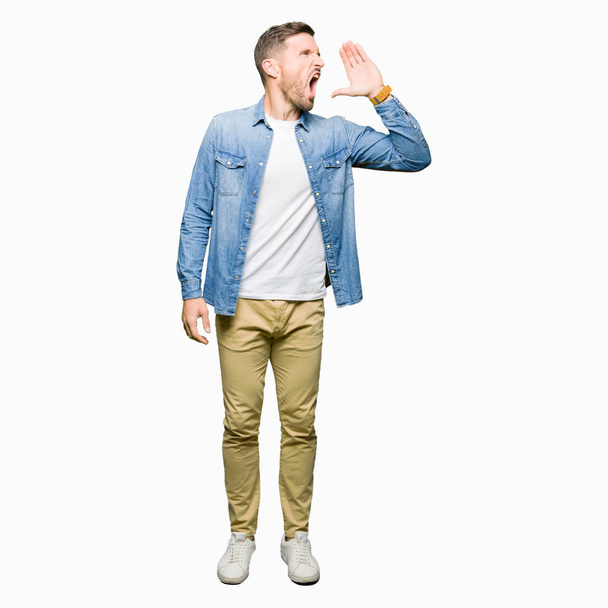 Handsome man with blue eyes and beard wearing denim jacket shouting and screaming loud to side with hand on mouth. Communication concept. - Foto, Bild