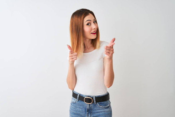 Beautiful redhead woman wearing casual t-shirt standing over isolated white background pointing fingers to camera with happy and funny face. Good energy and vibes. - Fotó, kép