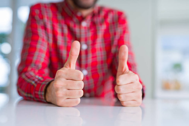 Закройте руки человек делает большой палец вверх жест над белым столом
 - Фото, изображение