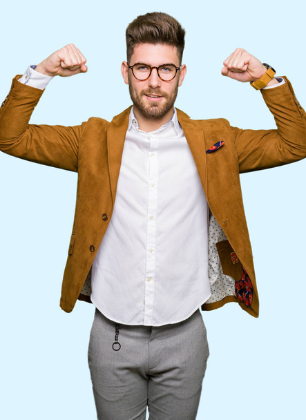 Young handsome business man wearing glasses showing arms muscles smiling proud. Fitness concept. - Photo, Image