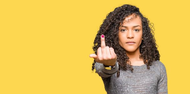 Young beautiful woman with curly hair wearing grey sweater Showing middle finger, impolite and rude fuck off expression - Fotoğraf, Görsel