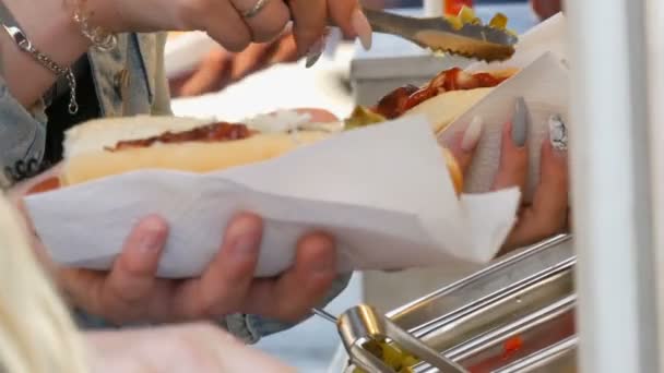 Дівчата руками ставлять різні приправи на хот-дог в спеціальному кіоску вуличної їжі, фаст-фуд на вулиці Амстердам. - Кадри, відео
