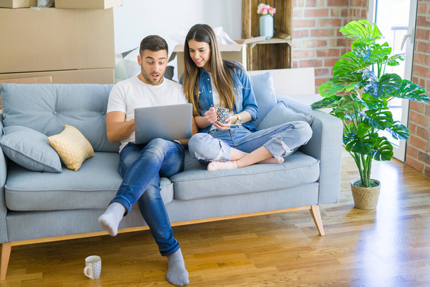 Jeune couple déménageant dans une nouvelle maison détente assis sur le canapé à l'aide d'un ordinateur portable, souriant heureux de déménager dans un nouvel appartement
 - Photo, image