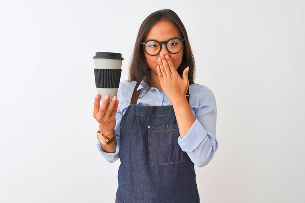 孤立した白い背景カバー口の上にコーヒーを持つ若い中国のバリスタ女性は、間違い、恐怖の表現、沈黙の中で怖がって、秘密の概念でショックを受けた手でコーヒーを持っています - 写真・画像