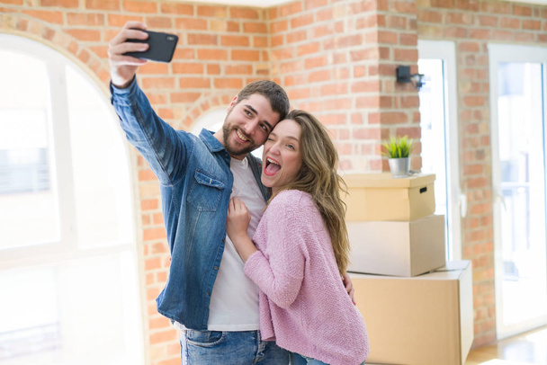 Nuori kaunis pari ottaa selfie-valokuvan älypuhelimella hymyillen erittäin onnellisena siirtymisestä uuteen kotiin
 - Valokuva, kuva