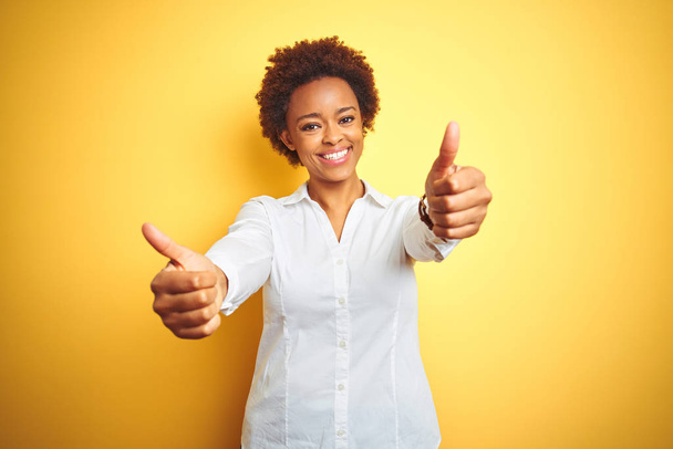 Afroamerikai üzleti nő több mint elszigetelt sárga háttér jóváhagyásáról csinál pozitív gesztus kézzel, remek mosolygott és boldog a sikerhez. Győztes kézmozdulat. - Fotó, kép