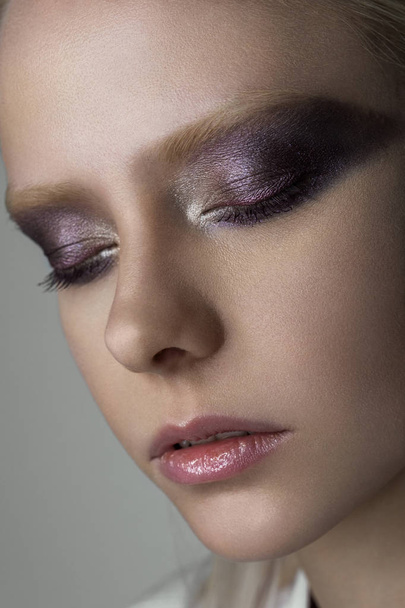 Close portrait of a platinum blonde with bright eye makeup in purple tones with a metallic glow. - Фото, изображение