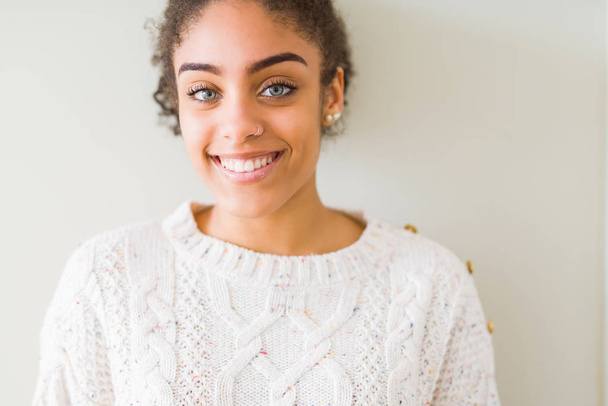 Belle jeune femme afro-américaine aux cheveux afro portant un pull décontracté avec un sourire heureux et cool sur le visage. Personne chanceuse
. - Photo, image