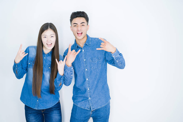 Beautiful young asian couple over white isolated background shouting with crazy expression doing rock symbol with hands up. Music star. Heavy concept. - Foto, afbeelding