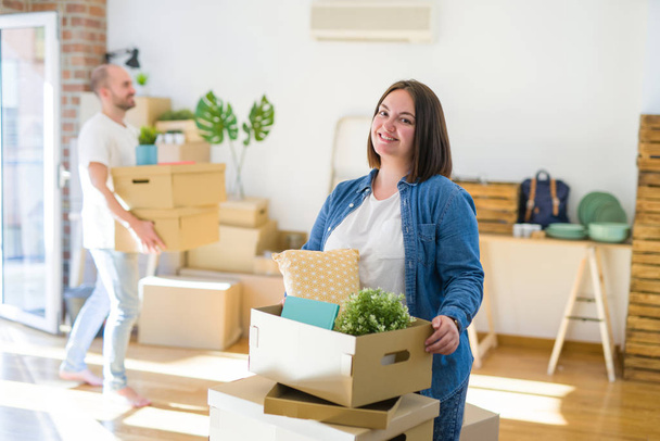 Молодая пара переезжает в новую квартиру, красивая женщина двигает картонные коробки и улыбается счастливой
 - Фото, изображение