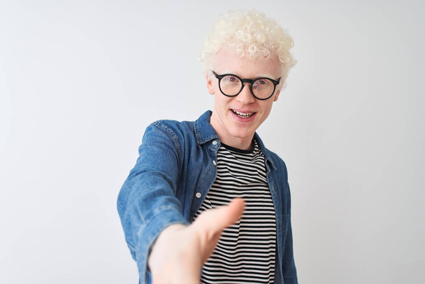 Mladý albín plavovlasý muž s džínovskou košilí a sklenicemi na izolované bílé pozadí s úsměvem, který nabízí stisk ruky jako pozdrav a přívětivý. Úspěšný obchod. - Fotografie, Obrázek