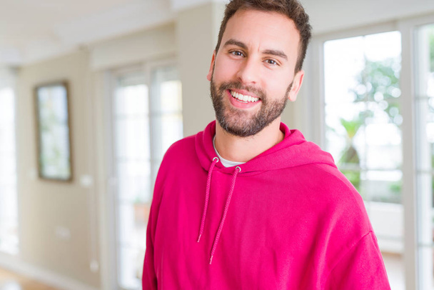 Knappe man dragen casual sweatshirt thuis en glimlachend poneren - Foto, afbeelding