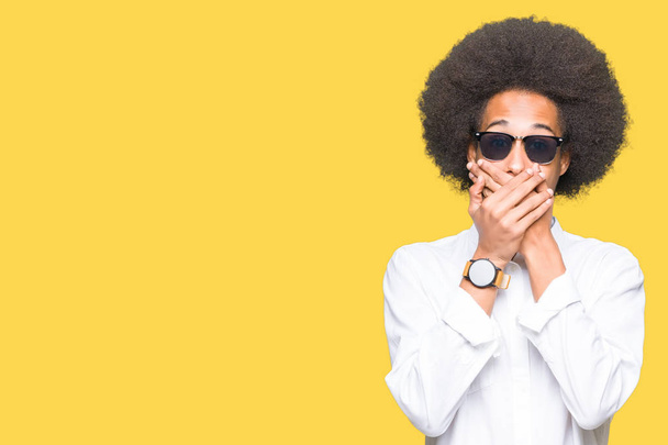 Young african american man with afro hair wearing sunglasses shocked covering mouth with hands for mistake. Secret concept. - Fotografie, Obrázek