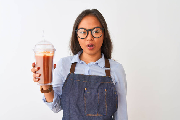Chinese woman wearing glasses apron drinking smoothie over isolated white background scared in shock with a surprise face, afraid and excited with fear expression - Photo, Image