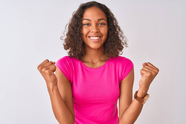 Young brazilian woman wearing pink t-shirt standing over isolated white background celebrating surprised and amazed for success with arms raised and open eyes. Winner concept. - Photo, Image