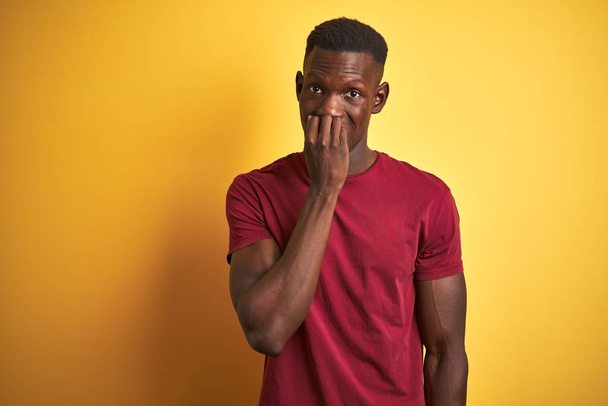 Giovane uomo afroamericano indossando t-shirt rossa in piedi sopra isolato sfondo giallo cercando stressato e nervoso con le mani in bocca mordere le unghie. Problema di ansia
. - Foto, immagini