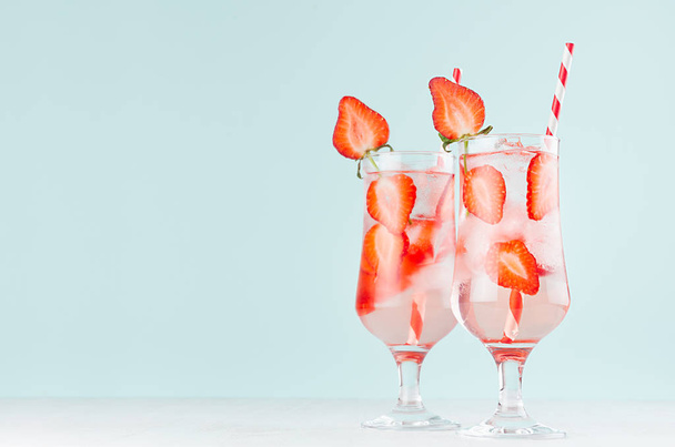 Bright cold strawberry cocktail with ripe red slices berry and sparkling water, ice cubes, red striped straw in misted glass in modern mint color interior. - Foto, imagen