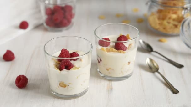 Yoghurt met framboos en granola geserveerd in een glazen pot. Gezond ontbijt van Cheerios volkoren granen met aardbeien confituur op houten tafel. - Video