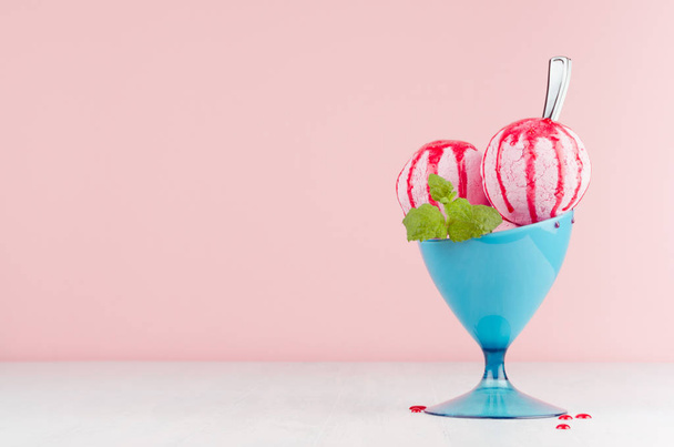 Tasty fresh pink ice cream in blue bowl with strawberry sauce, silver spoon, green mint on white wooden table and soft light pastel pink background. - Valokuva, kuva