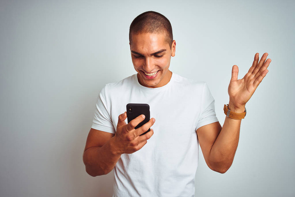 Mladý pohledný muž používající smartphone přes žlutý izolovaný podklad velmi šťastný a vzrušený, vítězný výraz oslavující vítězství s velkým úsměvem a zdvižným rukama - Fotografie, Obrázek