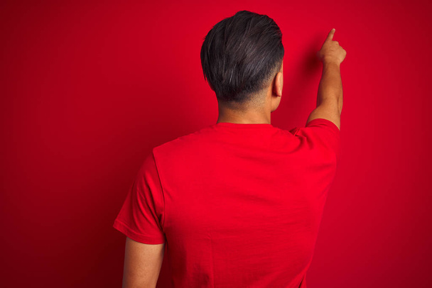 Jovem brasileiro vestindo camiseta em pé sobre fundo vermelho isolado Posando para trás apontando para a frente com a mão do dedo
 - Foto, Imagem