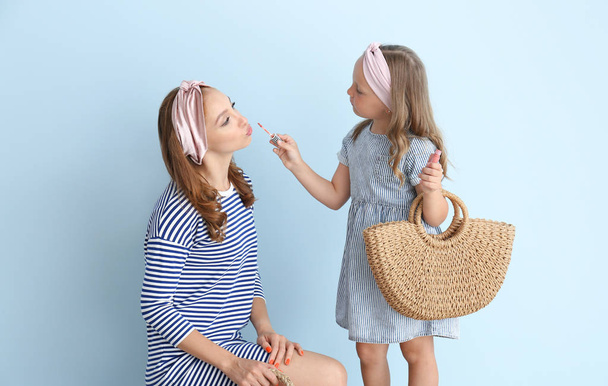Маленькая девочка наносит макияж на лицо матери на цветном фоне
 - Фото, изображение