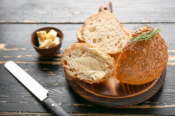 Tasty cut bun with butter on dark wooden table - Foto, Imagem