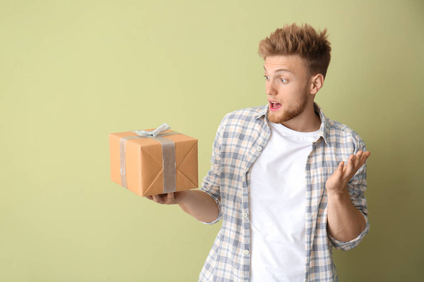 Έκπληκτος νεαρός άνδρας με κουτί δώρου στο φόντο χρώμα - Φωτογραφία, εικόνα