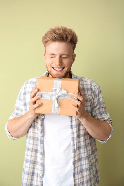 Щасливий молодий чоловік з подарунковою коробкою на кольоровому фоні
 - Фото, зображення