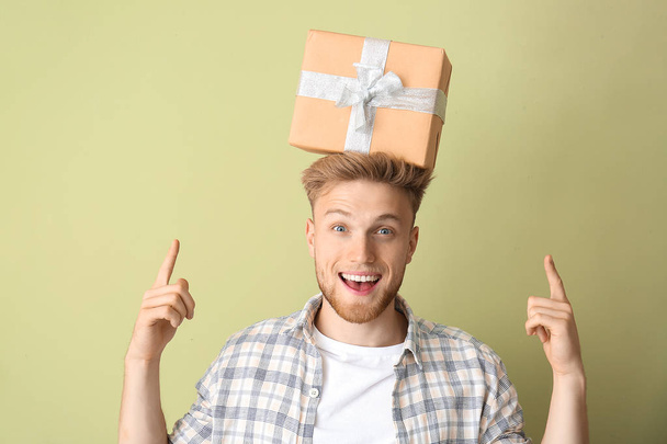 Joyeux jeune homme avec boîte cadeau sur fond de couleur - Photo, image