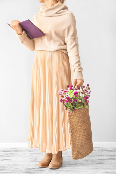 Woman with book and flowers in eco bag near light wall - Foto, Imagem