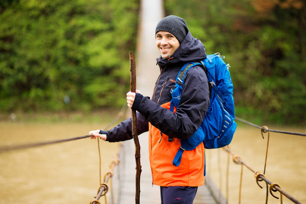 Homme avec sac à dos trekking dans la forêt par pont articulé sur la rivière. Le froid. Randonnée automnale. Pont en bois sur la rivière, Pont suspendu
 - Photo, image