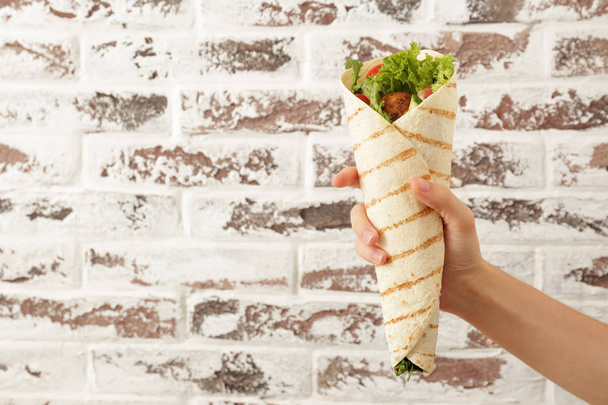 Female hand with tasty falafel pita against brick wall - Fotó, kép