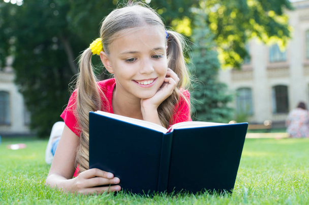 Schoolgirl read stories while relaxing green lawn. Cute pupil enjoy reading. School time. Interesting stories for kids. Study with pleasure. Time for great stories. Little child reading book outdoors - Фото, изображение