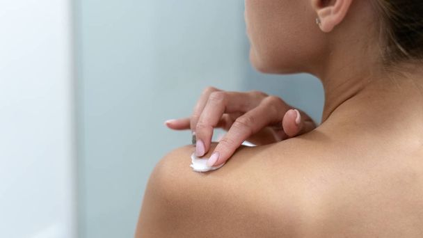 Женщина наносит крем для тела на плечи в ванной комнате
 - Фото, изображение