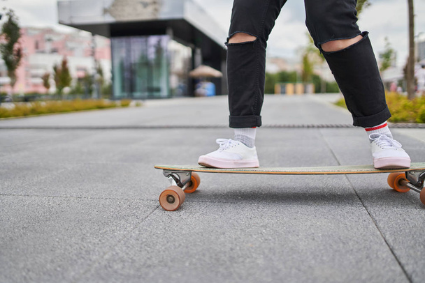Image of legs of woman in black jeans riding skateboard on street in city - 写真・画像