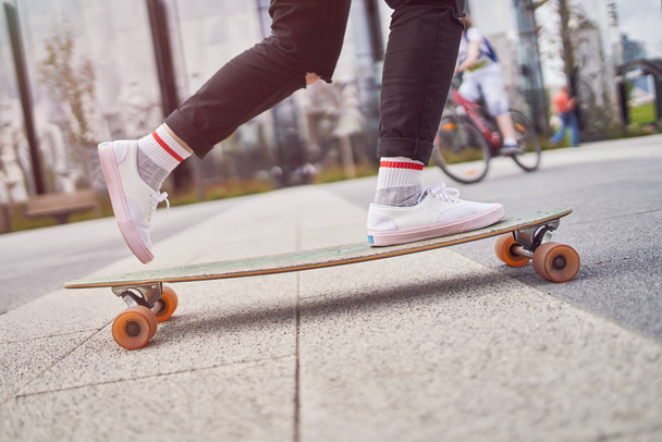 Picture of legs of woman in black jeans riding skateboard on street in city - Photo, Image