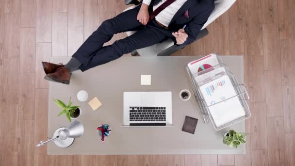 Вид зверху бізнесмена в костюмі, який залишається розслабленим з ногами на його офісному столі
 - Кадри, відео