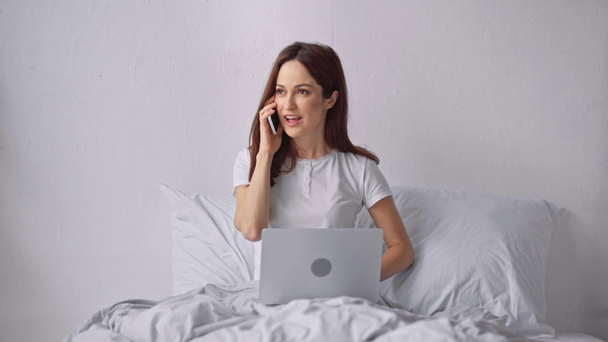 γυναίκα που χρησιμοποιεί φορητό υπολογιστή και μιλάει στο smartphone στο κρεβάτι - Πλάνα, βίντεο