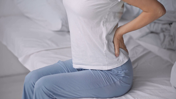 vista recortada de la mujer sentada en la cama con dolor de espalda
 - Imágenes, Vídeo