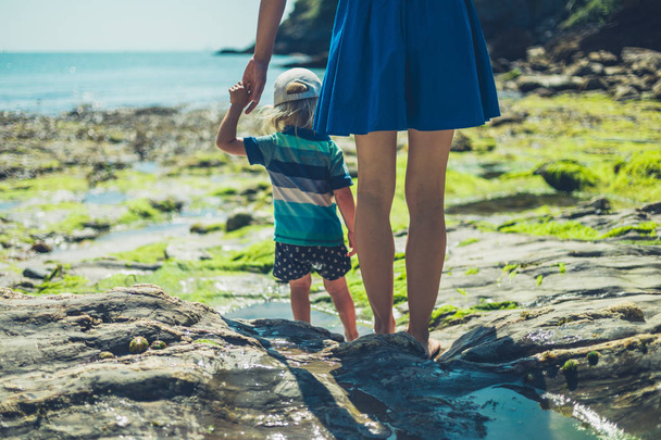 A young mother is walking on a rocky beach with her toddler on a sunny summer day - Foto, Imagem