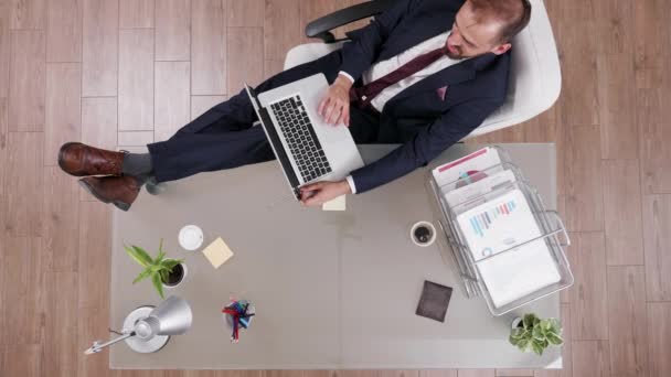 Vista superior del joven hombre de negocios en traje manteniendo sus pies en su escritorio de la oficina
 - Imágenes, Vídeo