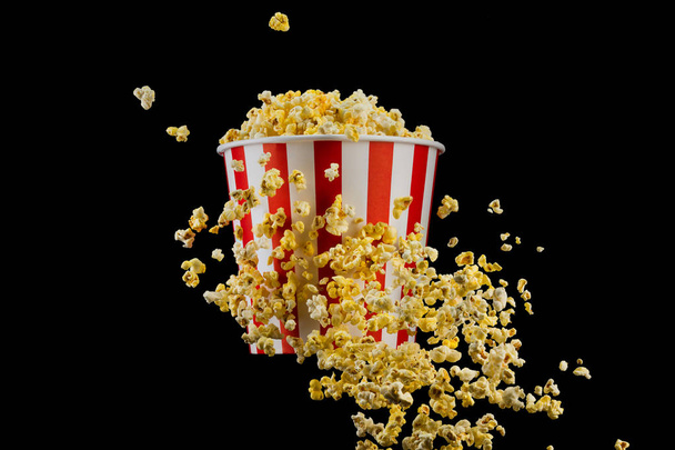 Flying popcorn from striped bucket isolated on black background - Photo, Image
