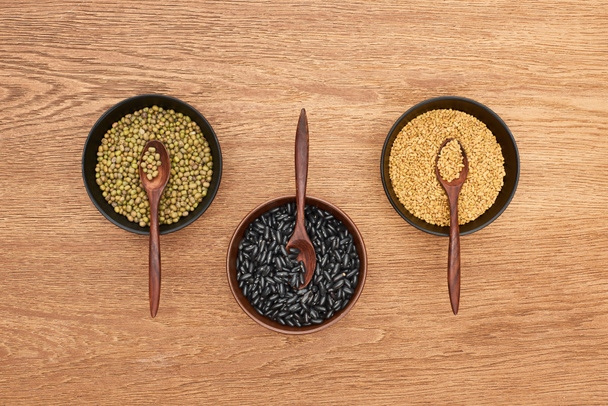 верхний вид чаш с различными бобами и зерном с ложками на деревянной поверхности
 - Фото, изображение